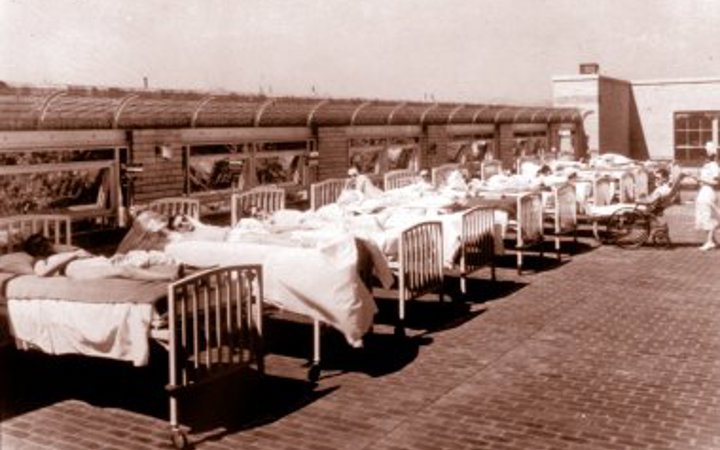 An old photo of 9 hospital beds lined up on the roof so the patients in them can get some sun