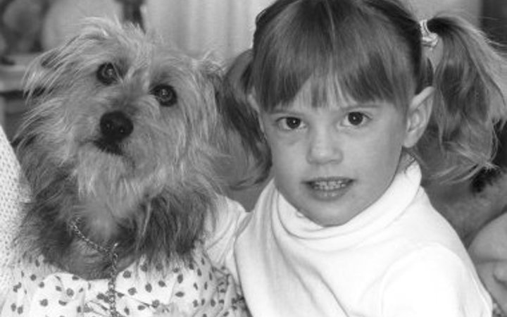 A black and white photo of a young girl with pigtails petting a small, shaggy dog