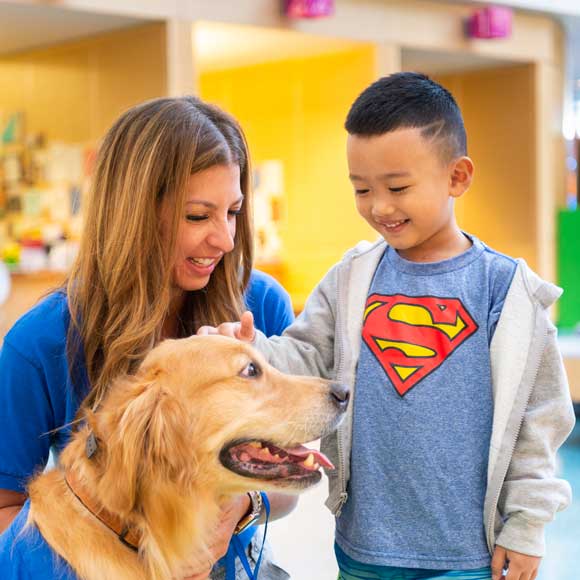Photo of a young boy smiling as he visits with a volunteer and her golden retriever in the Prescription Pet Program.