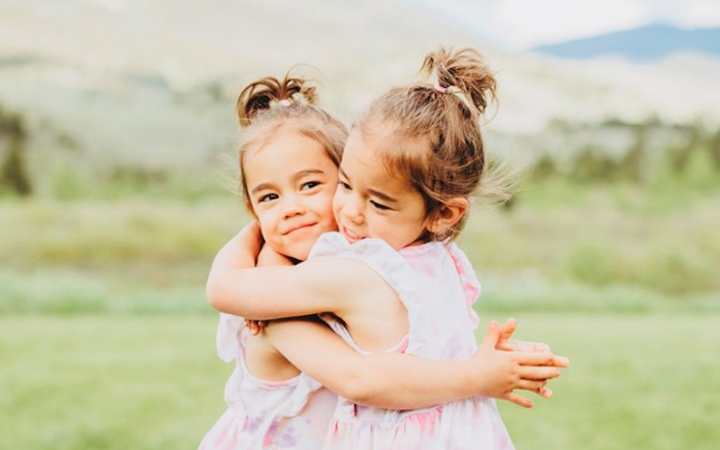 Zoey and Kenna hug tightly in front of a serene outdoor background