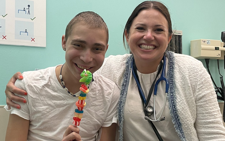 Seth smiles next to a provider in an exam room while he holds up a treat made of candies on a skewer. 