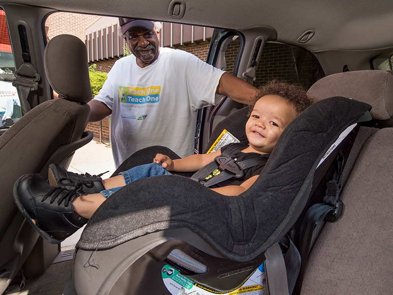 A man stands at the door of a minivan where a toddler is sitting in a car seat.