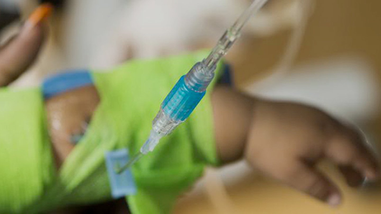 A close-up view of an IV inserted into a baby's arm that's wearing lime green bandages