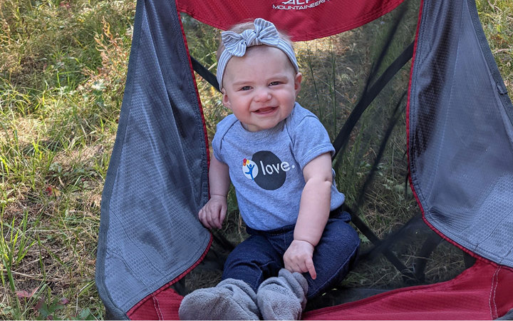 An infant girl sits smiling in a camping chair. She received care for fetal heart block at Children’s Colorado.