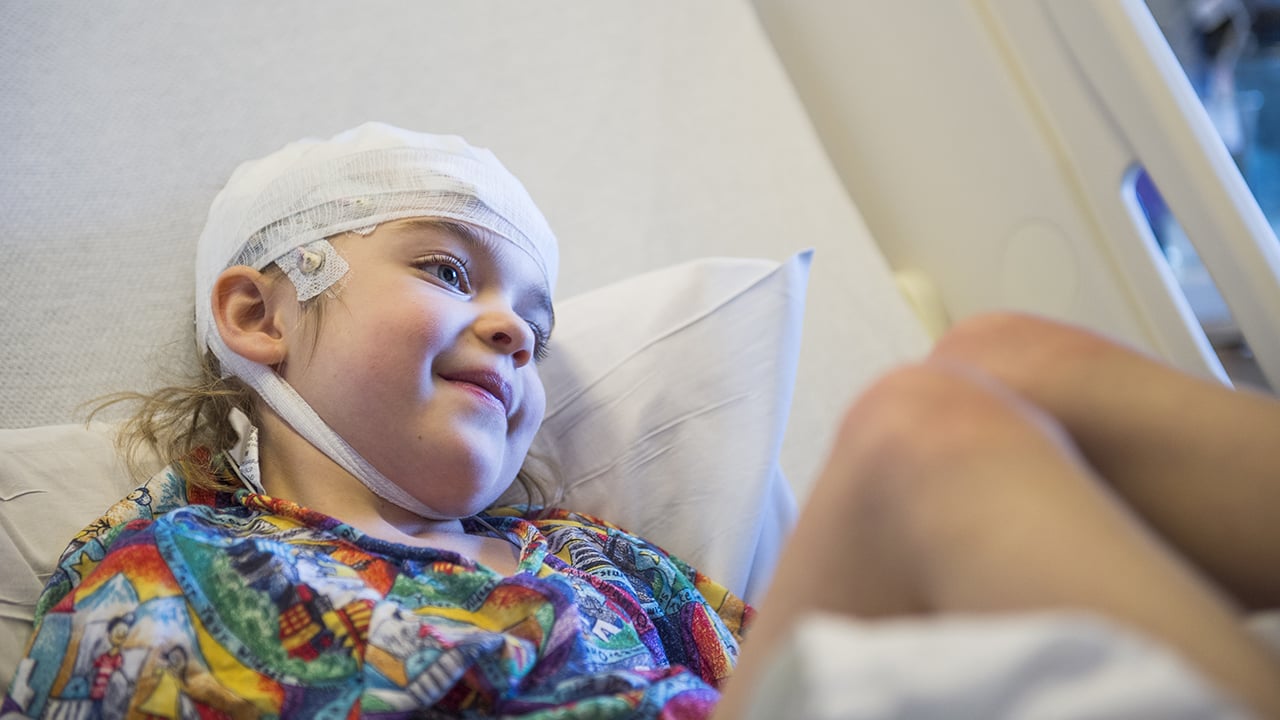 A kid lying in a hospital bed with bandages wrapped around her head