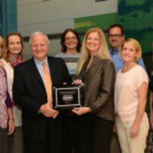 Eight people stand together posing with a plaque for Children's Hospital Colorado being a certified Duchenne care center.
