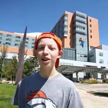 A boy in a Broncos jersey stands in front of the hospital.