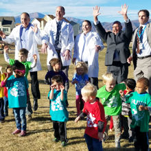 A group of doctors and kids stand in a mountain park cheering.
