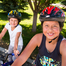 Two hispanic children smiling on their bikes in a park. 