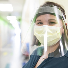 A nurse wearing a mask and face shield smiles at the camera. 