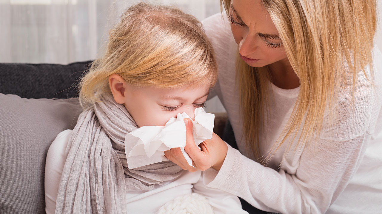A caregiver helps a young child blow their nose.