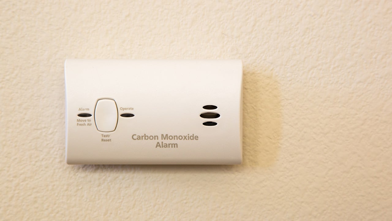 A white carbon monoxide alarm attached to a light beige wall.