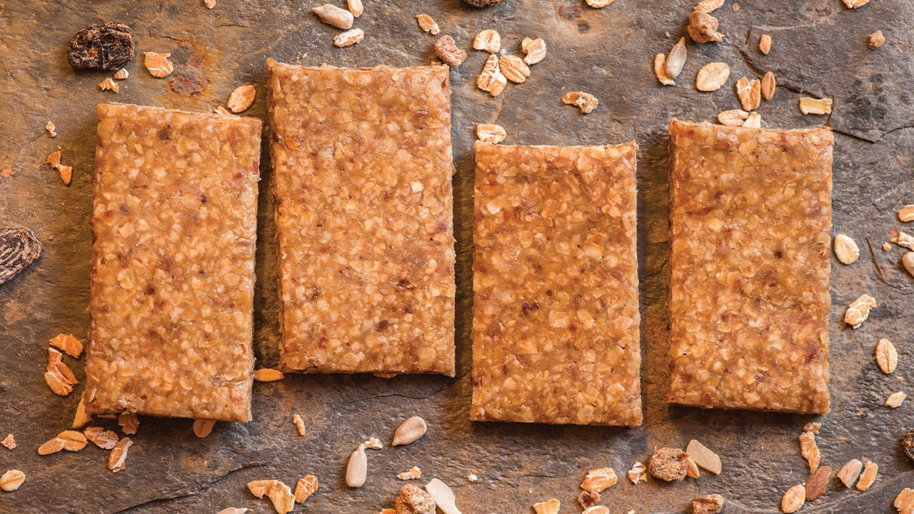 Four homemade energy bars for athletes that are a light brown color and made with oats and raisins.