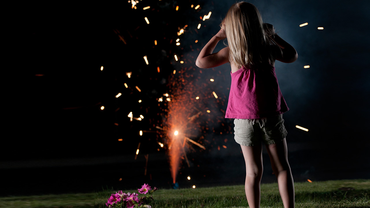 A young girl watches fireworks shoot up from the ground.