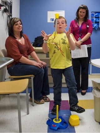 A boy tries to catch a toy rocket while his mom and a doctor watch in an examination room.