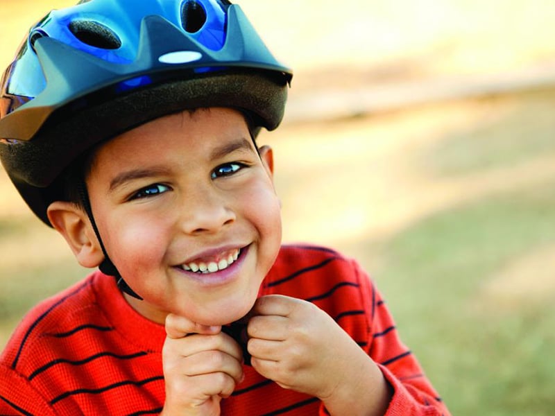 A boy is wearing a bike helmet and a red shirt with black stripes.