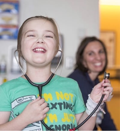 A girl in a green t-shirt plays with a stethoscope.