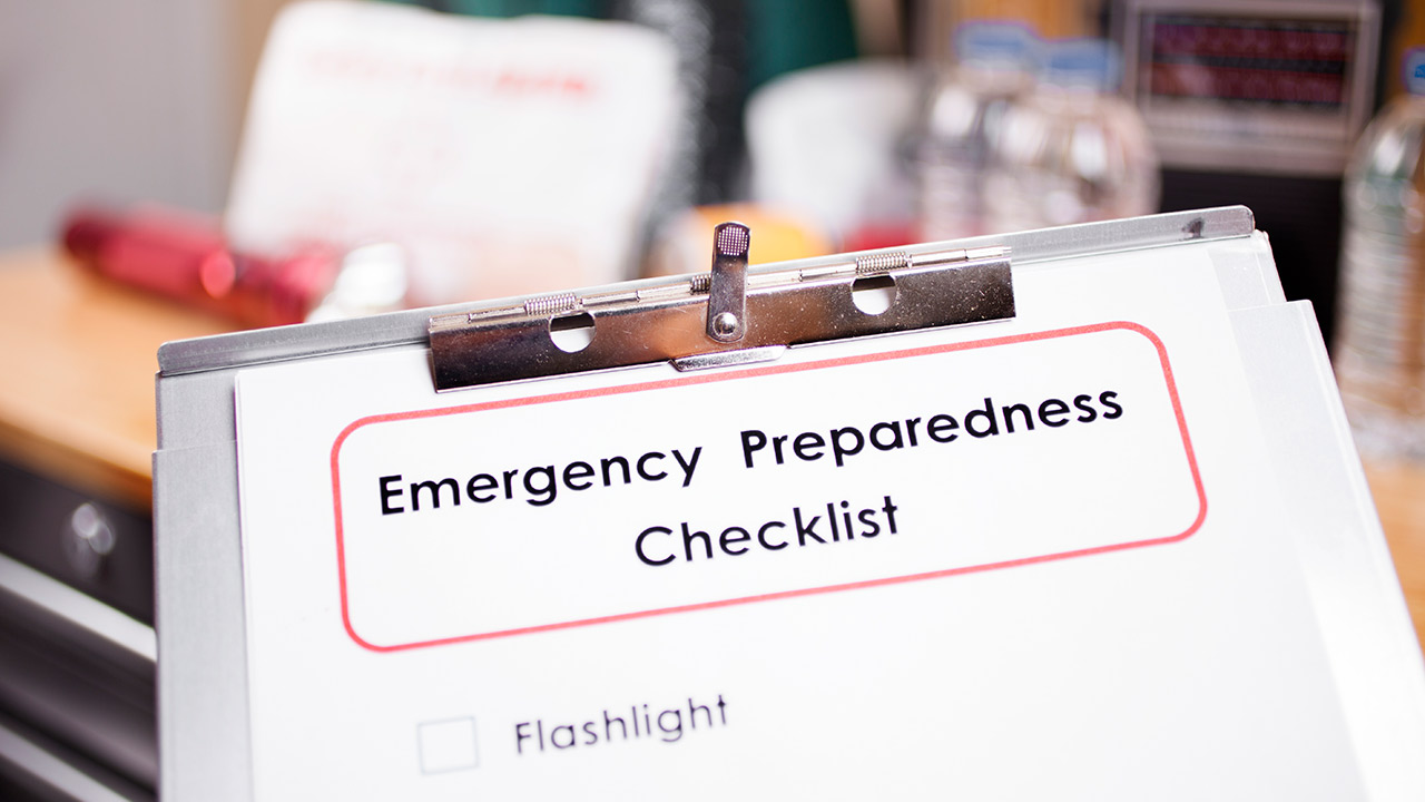 A clipboard with a paper that says Emergency Preparedness Checklist circled in red and the first item on the list is Flashlight.