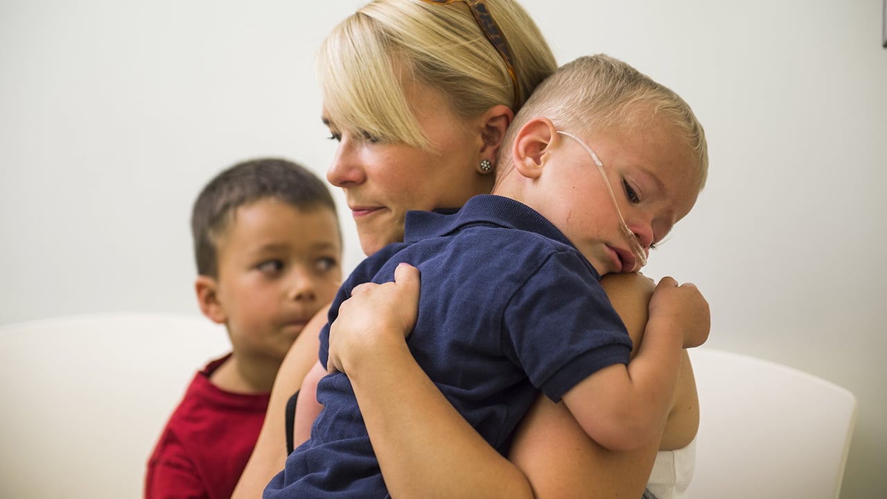 A mom holds her ill child while another boy sits next to her.