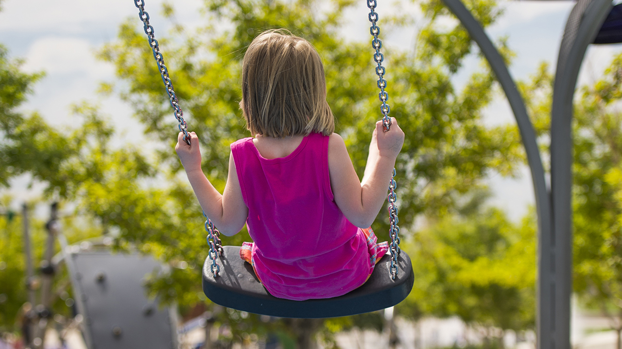 A girl swinging on the playground in the summer.