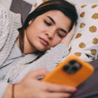 A teenage girl lies in bed while looking at her phone