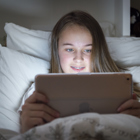 Teen girl looks at tablet at night in bed.