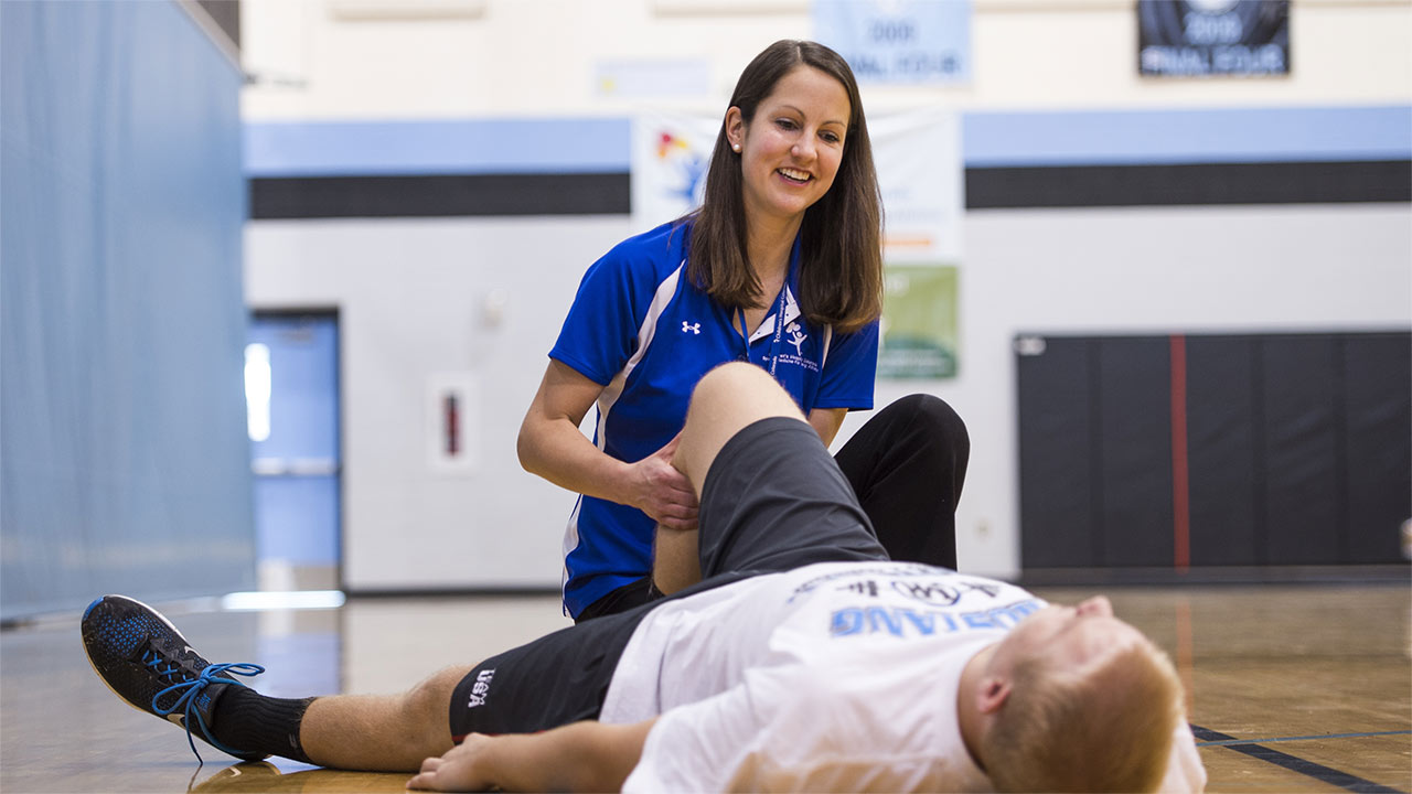 An athletic trainer checks a young male athletes knee after a knee injury.