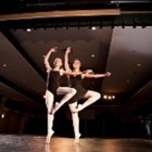 Two ballerinas dance on pointe in a theater.