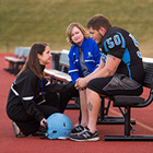 A football player sits on a bench while two women talk to him.