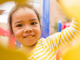 A young girl in a yellow and white striped shirt plays in a jungle gym.
