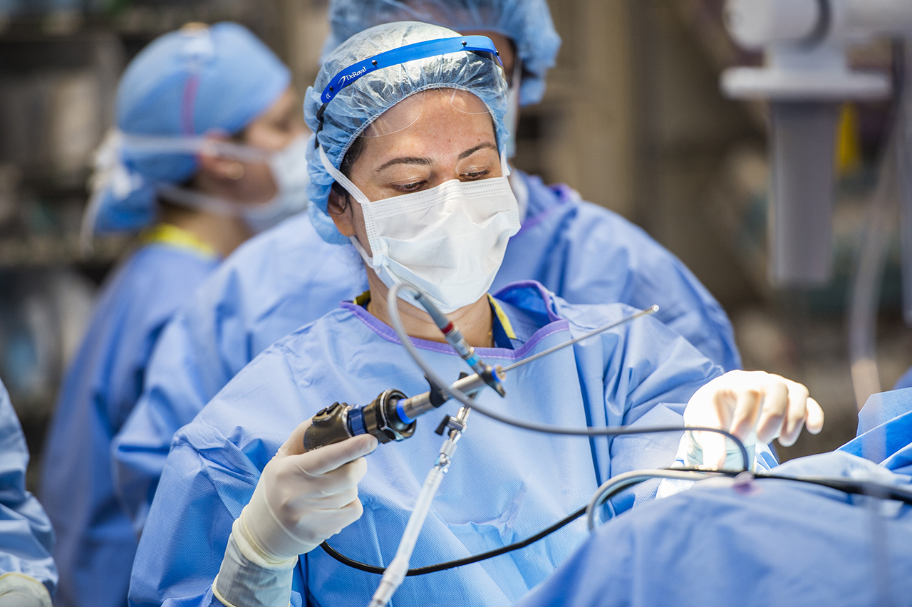 Dr. Bischoff is in the operating room, holding a surgical tool and doing surgery. 