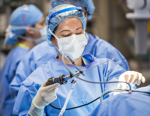 Dr. Bischoff is in the operating room, holding a surgical tool and doing surgery. 