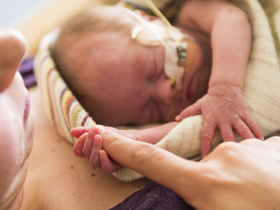 Newborn with oxygen holds finger of mother while laying on her chest