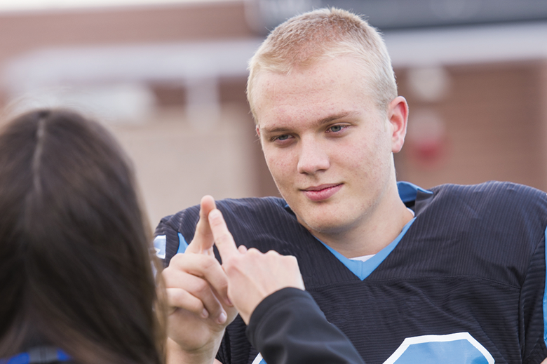 Teenaged football player touching index fingers with athletic trainer