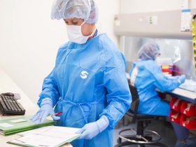 Researchers working with papers in blue scrubs and protective headgear.